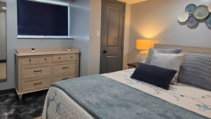 A bedroom with a bed, dresser, window, door, and wall decor. - The Hideaway | Cozy 2BR Retreat in Pontiac (Pontiac)