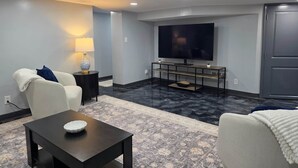A modern living room with a flat-screen TV, a sofa, a coffee table, and a patterned rug. - The Hideaway | Cozy 2BR Retreat in Pontiac (Pontiac)