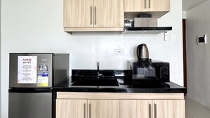 A modern kitchen with light wood cabinets, a stainless steel refrigerator, a black stove, and a microwave. - Royal Oceancrest Panglao 1 (Dauis)