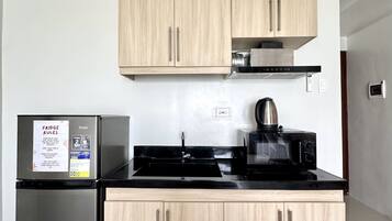 A modern kitchen with light wood cabinets, a stainless steel refrigerator, a black stove, and a microwave.
