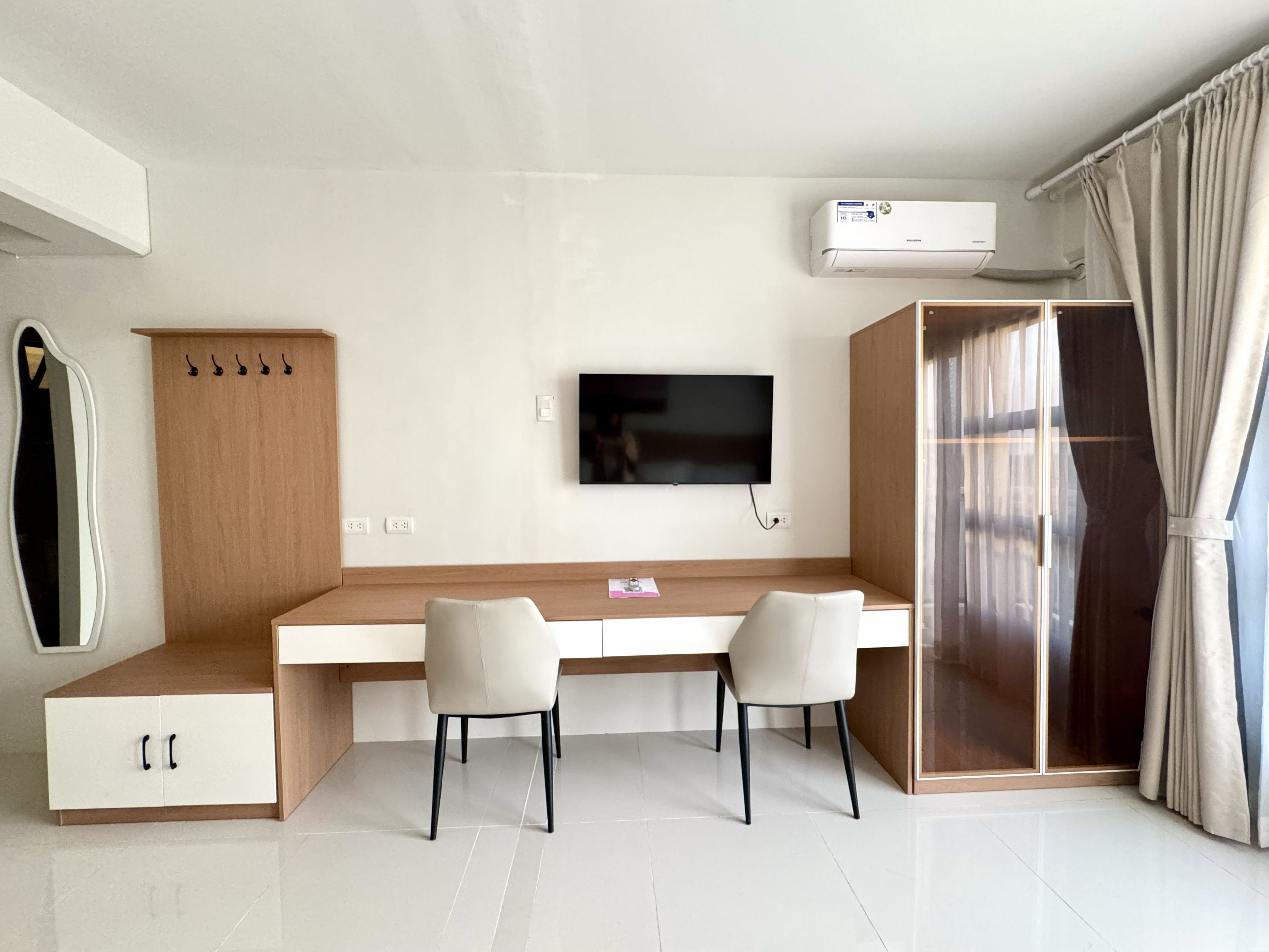 A modern bedroom with a bed, a desk, two chairs, a TV, and an air conditioning unit.