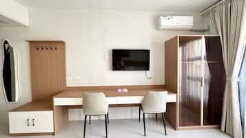 A modern bedroom with a bed, a desk, two chairs, a TV, and an air conditioning unit.