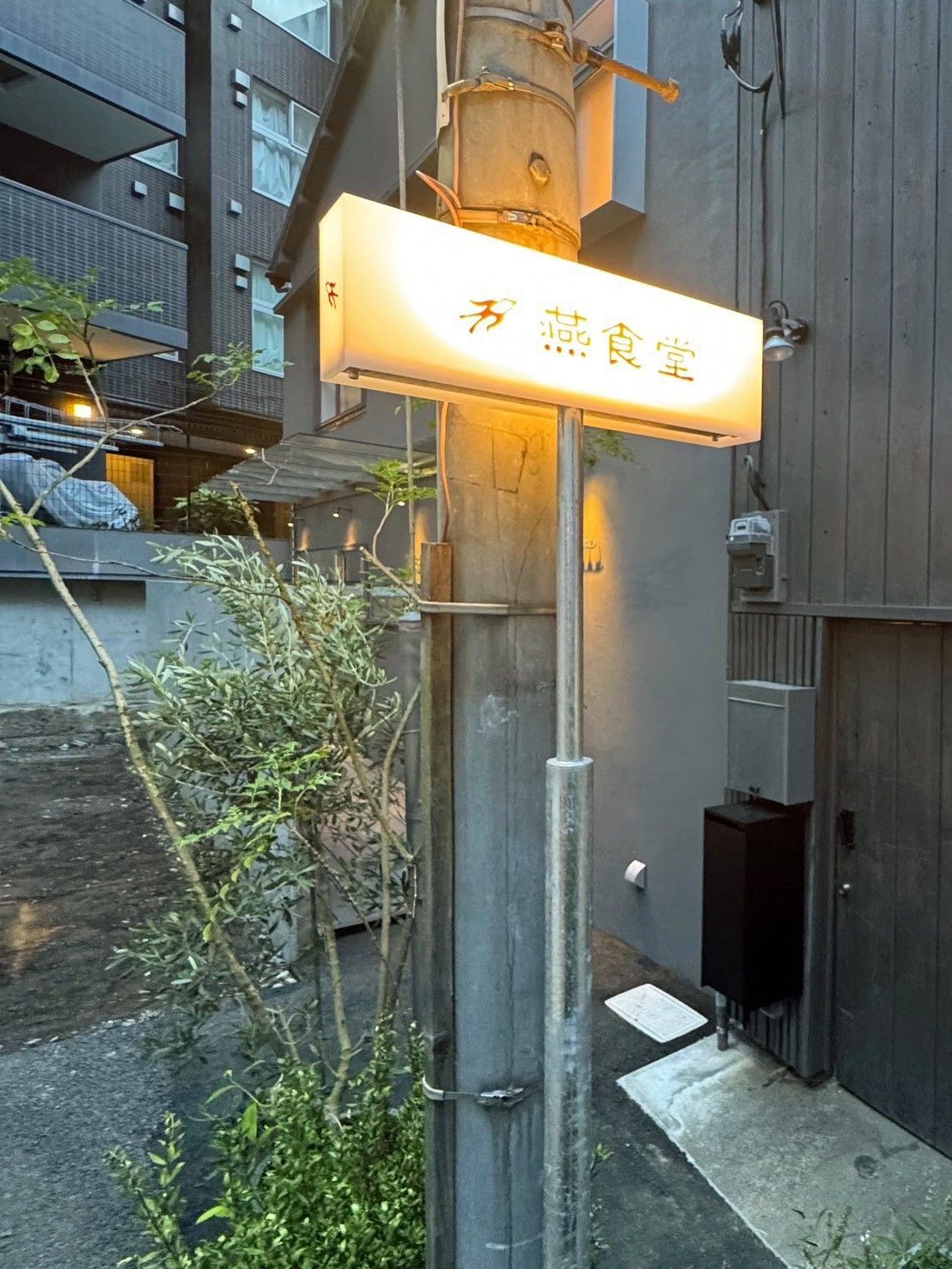 A sign with Japanese characters, a metal pole, and a building with a gray facade.