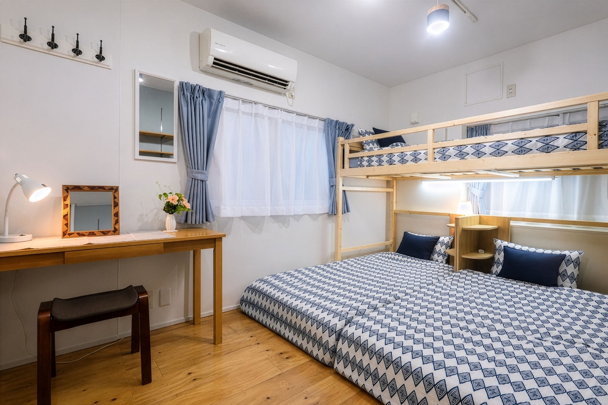 Una habitación con literas, un escritorio con espejo, una lámpara y una ventana con cortinas.