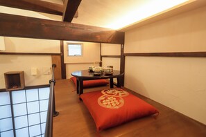 Una habitación con piso de madera, una mesa con un cojín rojo, una ventana y un estante pequeño con un objeto rojo.