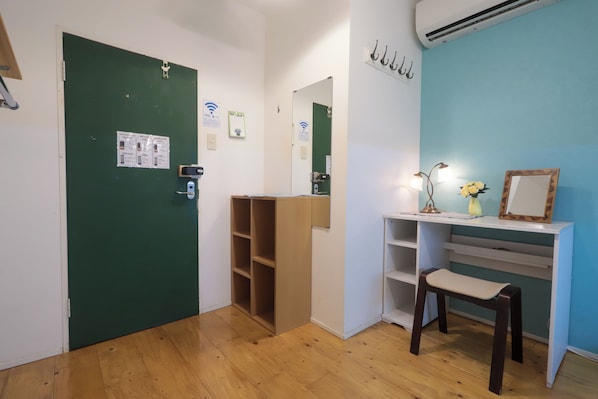 Una habitación con puerta verde, pared blanca, suelo de madera, un escritorio con una silla y un espejo.