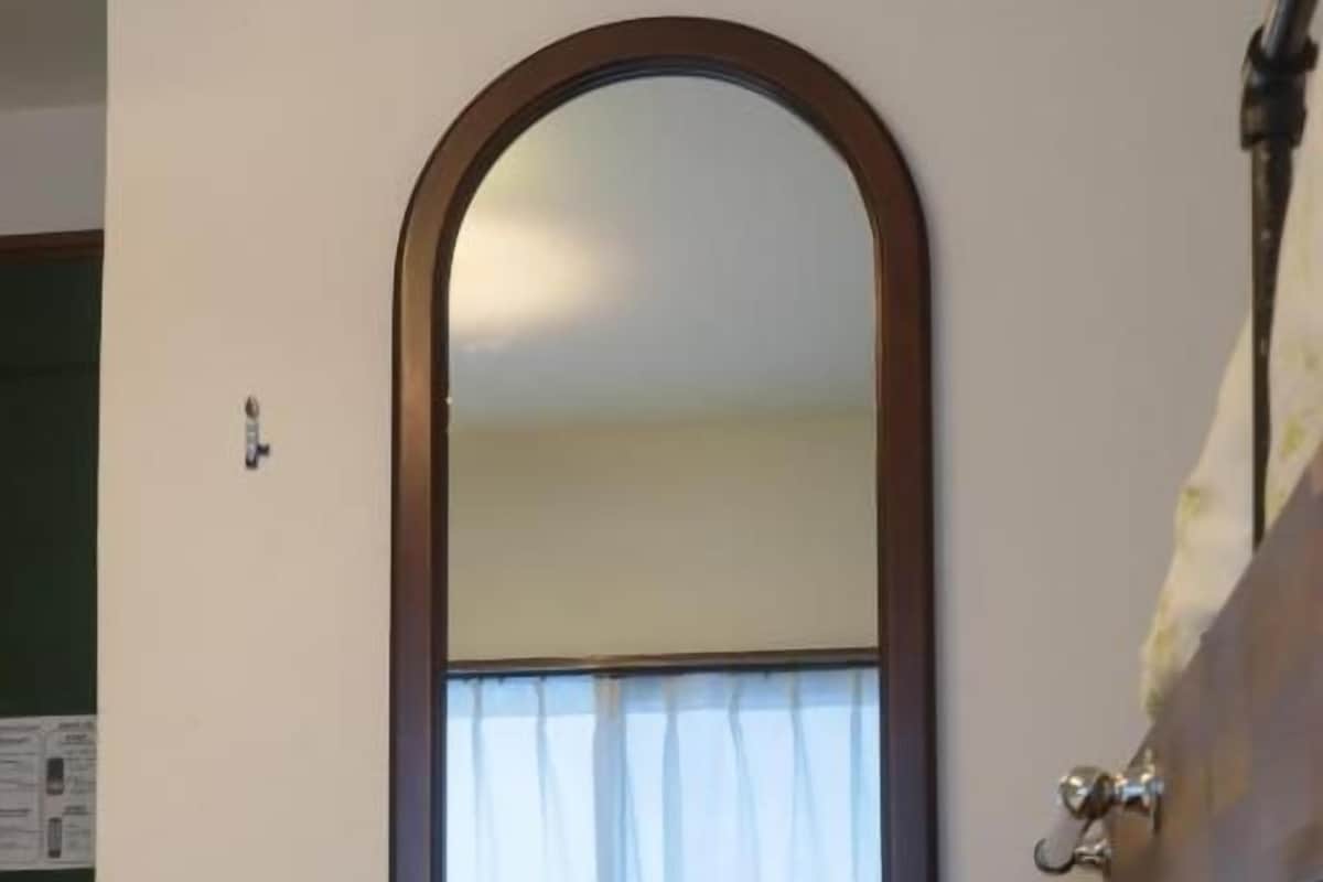 A bedroom with a large mirror, a bed with a white bedspread, and a window with curtains.