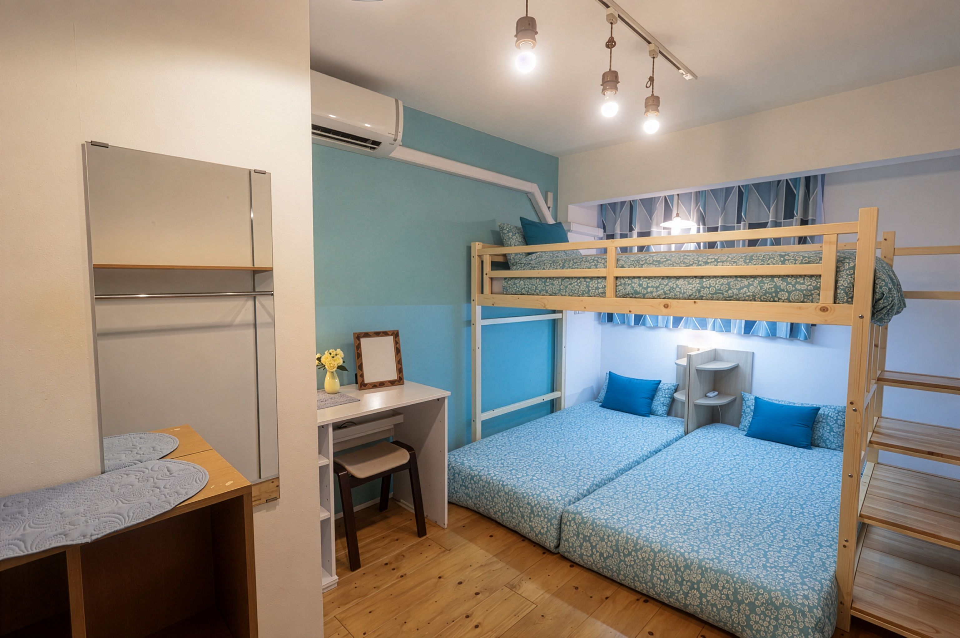 A bunk bed room with a desk and chair, a small table with a lace tablecloth, and an air conditioning unit.