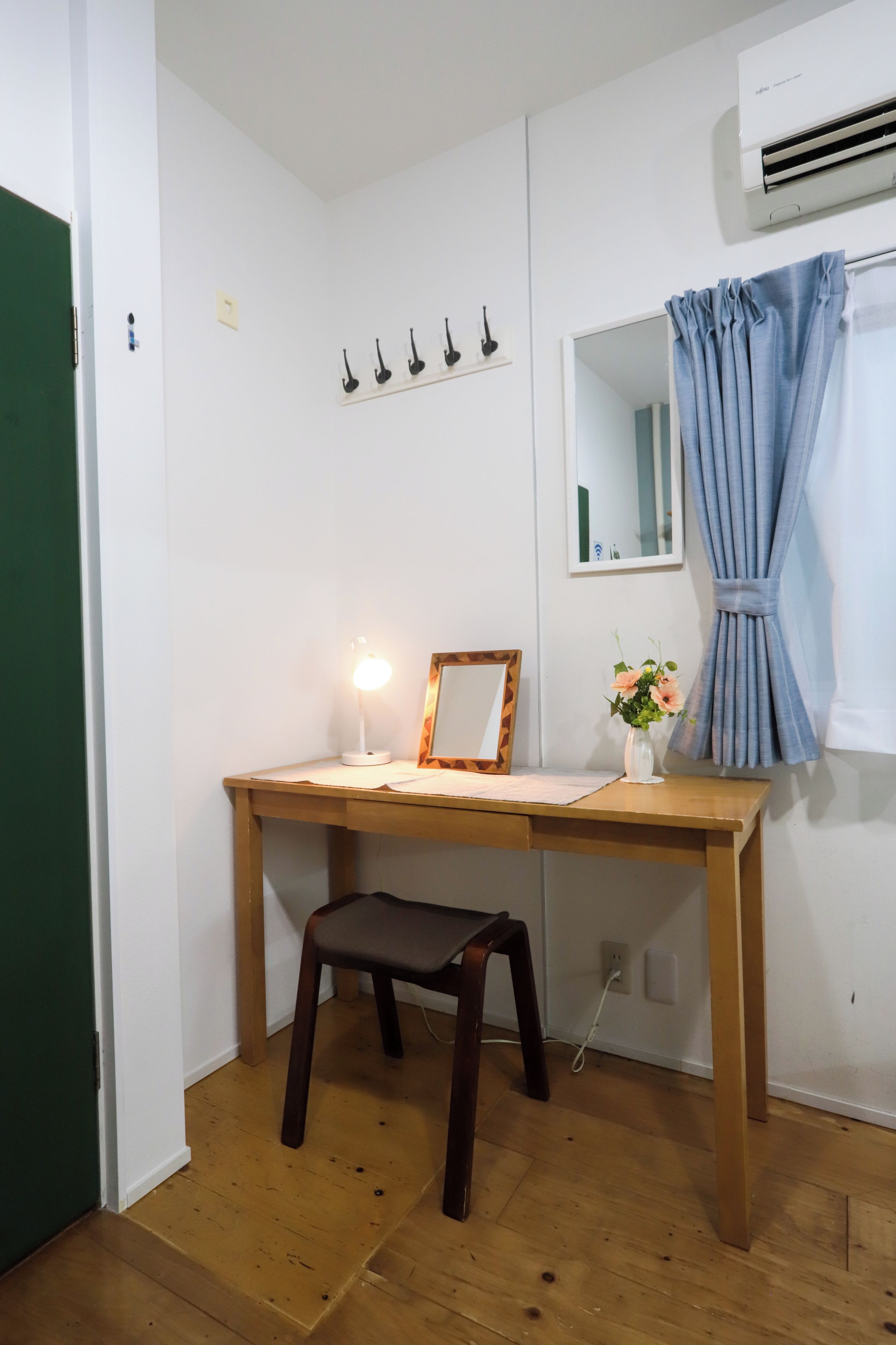 A small room with a wooden desk, a chair, a mirror, a lamp, and a window with curtains.
