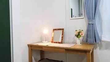A small room with a wooden desk, a chair, a mirror, a lamp, and a window with curtains.