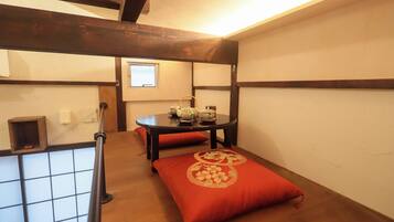 A room with a wooden floor, a table with a red cushion, a window, and a small shelf with a red object.