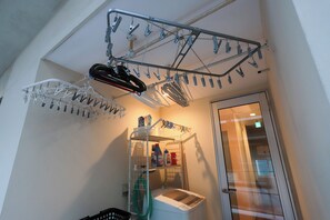 Un área de lavandería con un tendedero, una lavadora y un estante con productos de limpieza.