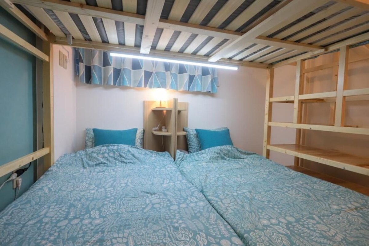 A room with a bed, a bedside table, and a wall-mounted shelf.