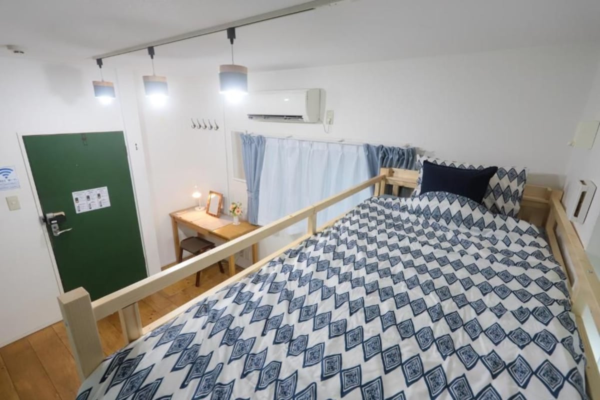 A bedroom with a bed, a desk, a chair, and a green door.