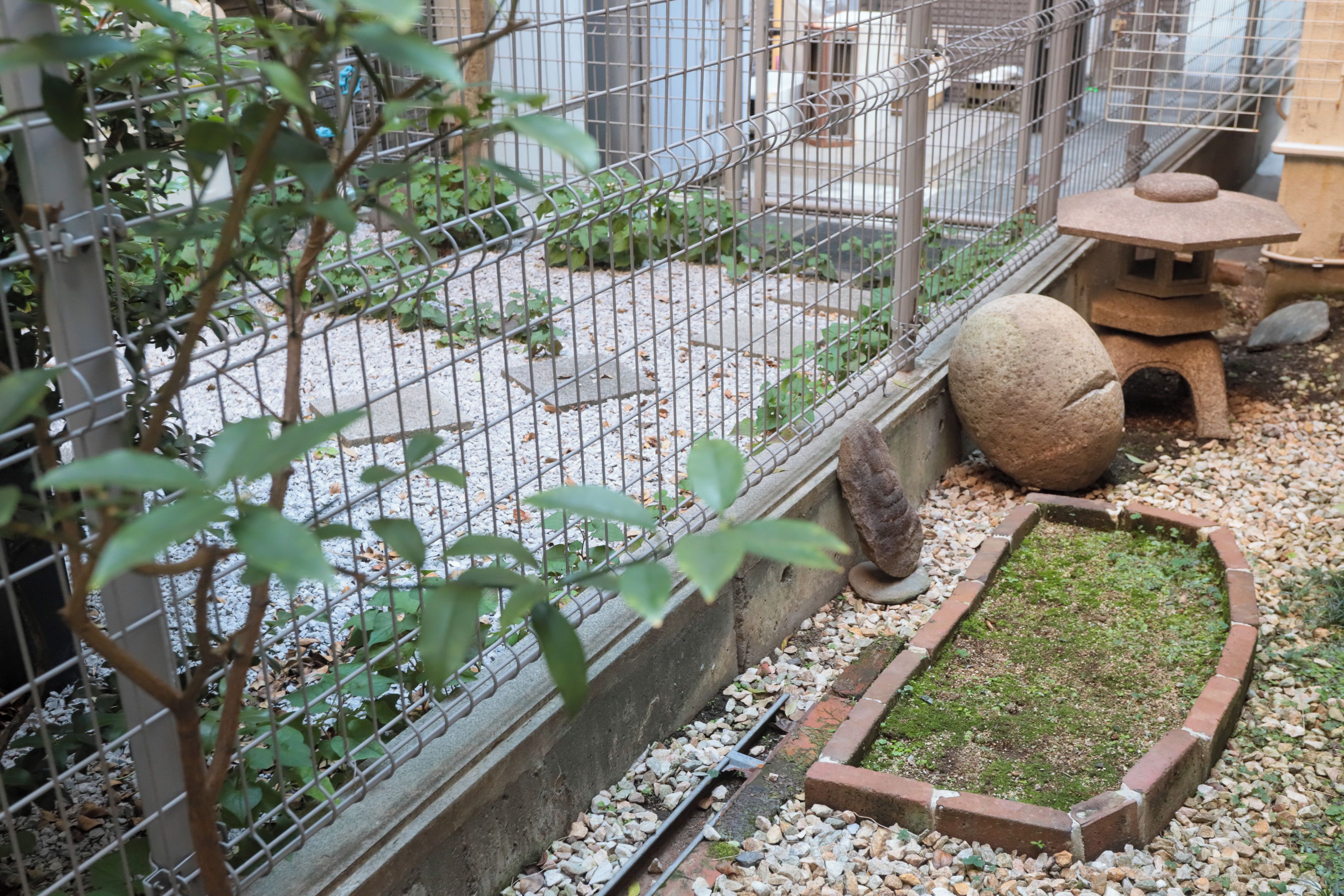 Un jardín con un farol de piedra, un pequeño estanque y una valla de metal.