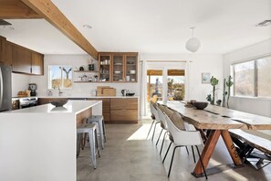 Eine moderne Küche mit einer zentralen Kochinsel, weißen Schränken und einem Essbereich mit Holztisch und weißen Stühlen.