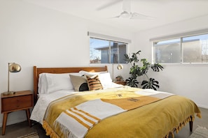 Ein Schlafzimmer mit Bett, Nachttisch, Lampe und großen Fenstern.