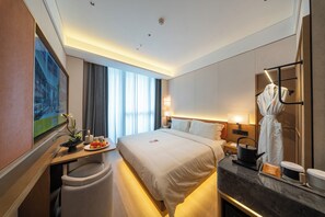 A hotel room with a bed, bedside table, lamp, robe, and a mirror. - SSAW Boutique Hotel Shenzhen Snow World (Shenzhen)