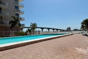 Ein Schwimmbecken mit gepflastertem Weg, einer Brücke und einem Gebäude mit Balkonen im Hintergrund.
