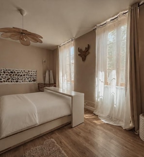 A bedroom with a bed, a ceiling fan, a window with curtains, and a wall-mounted decorative piece.