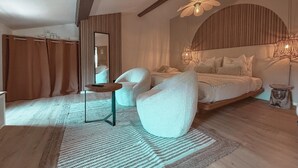 Une chambre moderne avec un grand lit, un coin salon avec une petite table et un grand miroir.