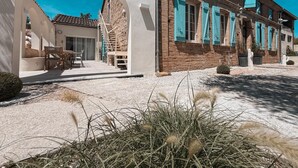 Il s'agit d'un bâtiment traditionnel doté d'une façade en pierre, de volets bleus et d'une arche blanche qui mène à un patio aménagé avec du mobilier d'extérieur.