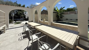 Une terrasse extérieure avec une table et des chaises, une piscine et un mur en pierre.