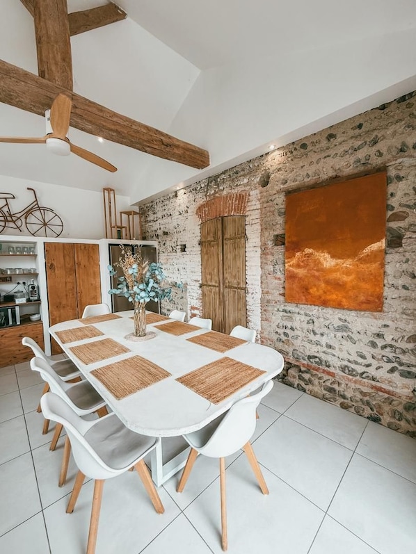 A dining area with a white table set for six, surrounded by white chairs with wooden legs.