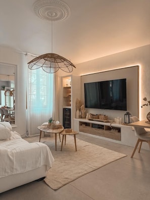A modern living room with a large flat-screen TV, a bed, a dining area, and a ceiling light fixture.