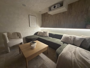 A modern living room with a sofa, a chair, a coffee table, and a wall-mounted projector.