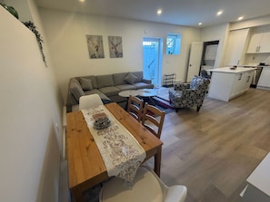 Ein modernes Wohnzimmer mit Essbereich, einer Couch, einem gemusterten Sessel und einer Küchenzeile.