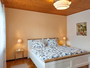 Ein Schlafzimmer mit Holzboden, einem Bett mit floralem Bettzeug, zwei Nachttischlampen und einem Gemälde an der Wand.