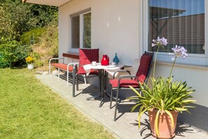 Eine Terrasse im Freien mit Tisch, Stühlen, einer Topfpflanze und einem Fenster.