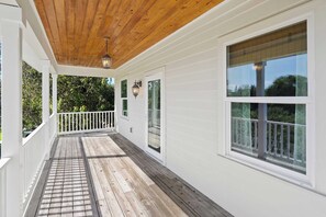 Eine überdachte Veranda mit Holzboden, weißem Fassadenholz und Blick auf Bäume.