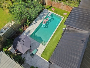 Ein rechteckiger Swimmingpool mit einer gefliesten Liegefläche, umgeben von einem Holzzaun und einer Rasenfläche.