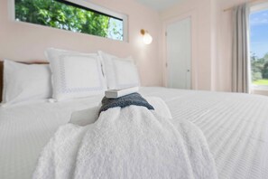 Ein ordentlich bezogenes Bett mit Kissen und Decke, eine Nachttischlampe und ein Fenster mit Blick auf Grünflächen.