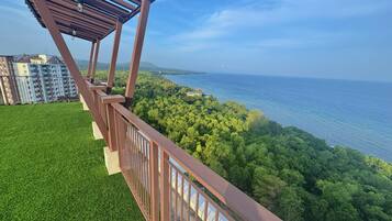 A balcony with a view of a coastal landscape, including a body of water and a forested area.
