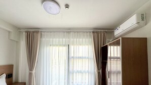 A hotel room with a bed, a wardrobe, a desk, and a window with curtains. - Royal Oceancrest Panglao 1 (Dauis)