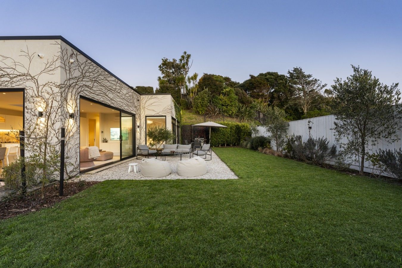 Uma casa moderna com porta de entrada de vidro, um pátio com móveis de exterior e um gramado bem cuidado.