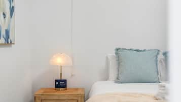 Um quarto com luminária de cabeceira, cama com travesseiro azul claro e uma obra de arte na parede.