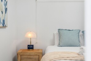 A bedroom with a bedside lamp, a bed with a light blue pillow, and a wall-mounted artwork. - The Ivy by Homello (Auckland)