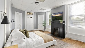 Een slaapkamer met een bed, een open haard, een televisie en een raam met zonwering.
