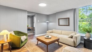 Een woonkamer met een bank, een salontafel, een lamp en uitzicht op groen.