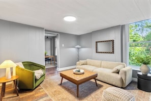 Ein Wohnzimmer mit einer Couch, einem Couchtisch, einer Lampe und Blick auf Grün.