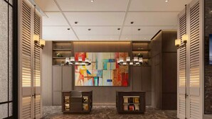 Un vestíbulo de hotel con piso de mármol, un cuadro abstracto de gran tamaño y dos mesas auxiliares con lámparas.