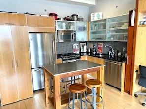 A modern kitchen with stainless steel appliances, wooden cabinets, and a bar stool area. - Williamsburg Loft w/fast Manhattan access (Brooklyn)
