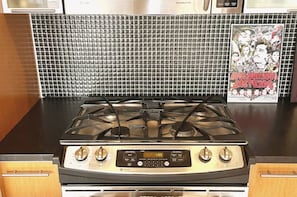 A kitchen with a gas stove, a digital clock, and a tiled backsplash. - Williamsburg Loft w/fast Manhattan access (Brooklyn)
