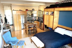 A compact room with a bed, a kitchenette, a small dining table with stools, and a blue chair. - Williamsburg Loft w/fast Manhattan access (Brooklyn)