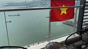 Un balcón con una bandera, vistas de un horizonte urbano y una masa de agua.