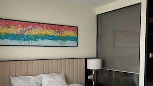 Una habitación de hotel con una cama grande, un cabecero, una mesita de noche con lámpara y un cuadro en la pared.